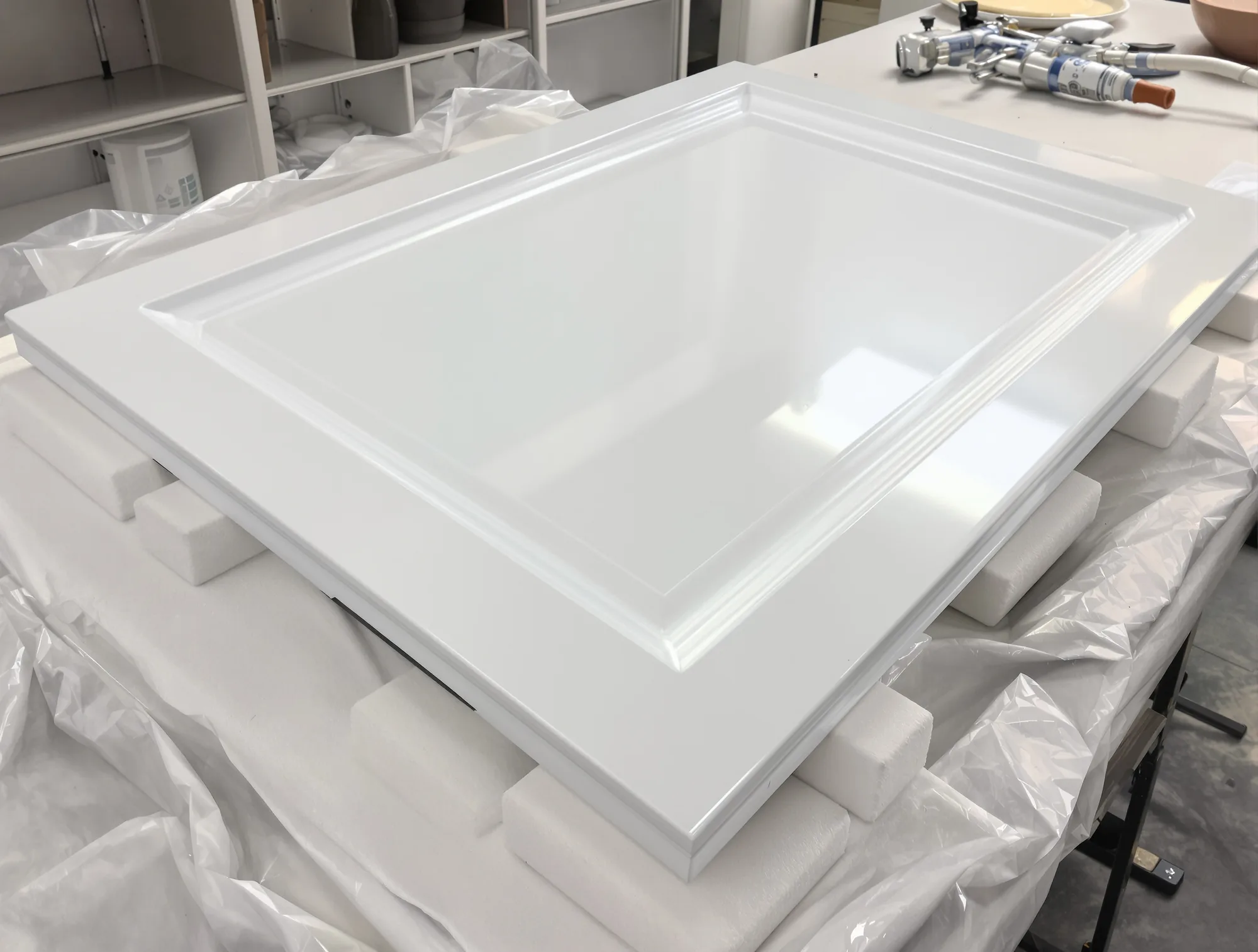 Cabinet door lying flat on padded stands with a fresh, glossy sprayed white finish