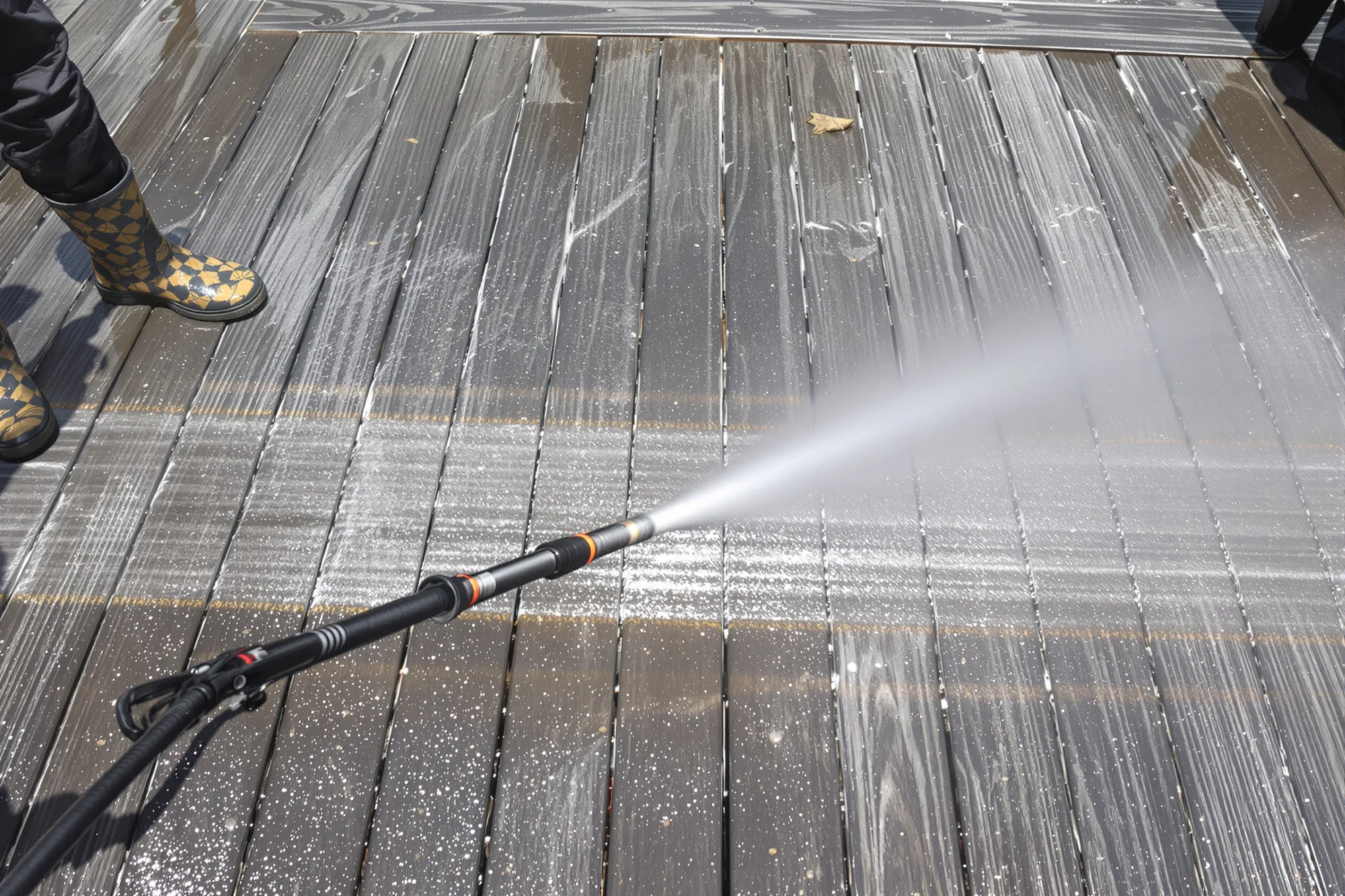 Pressure washer leaving a clean stripe across dirty gray deck boards