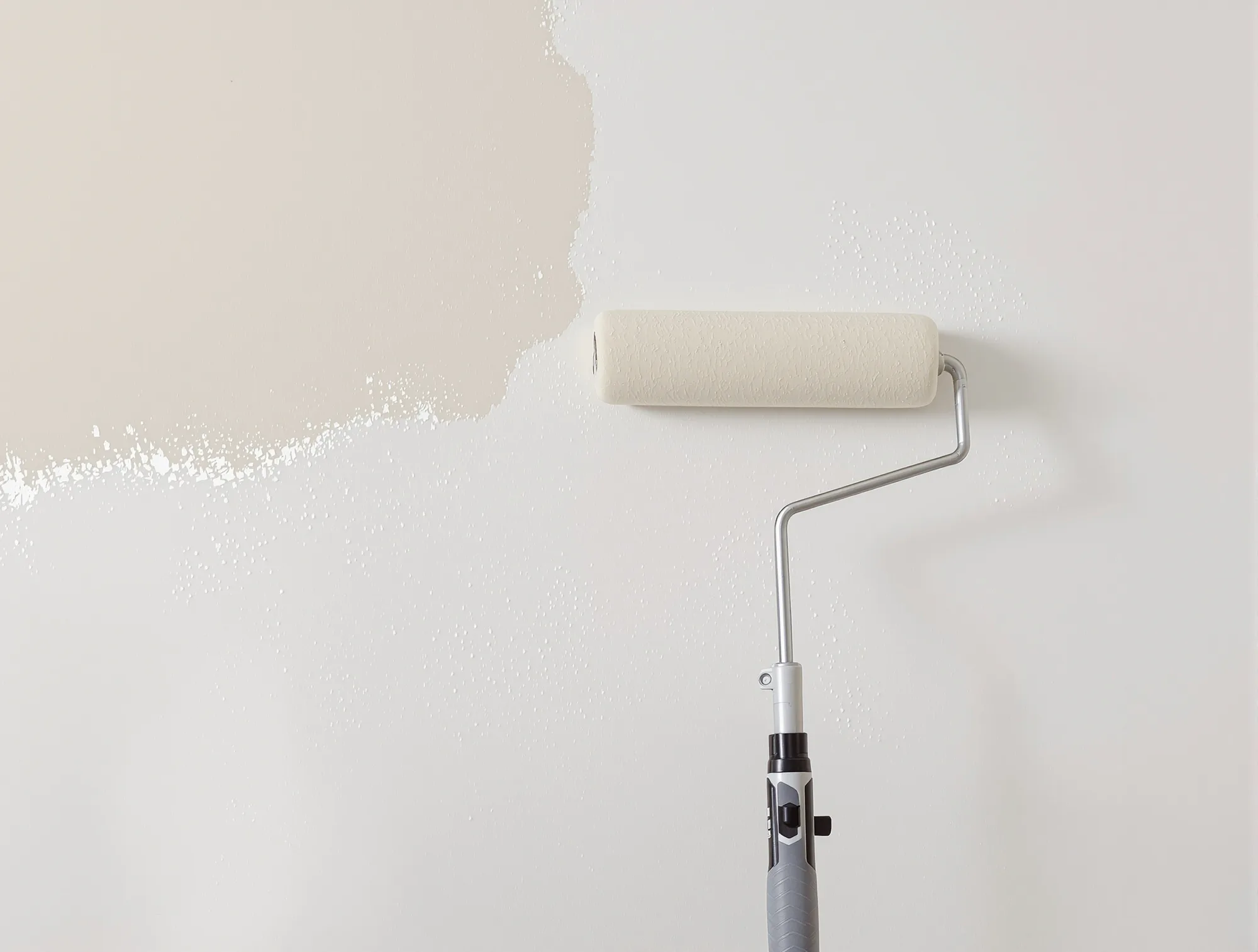 Roller on a pole rolling warm white paint over a repaired wall section