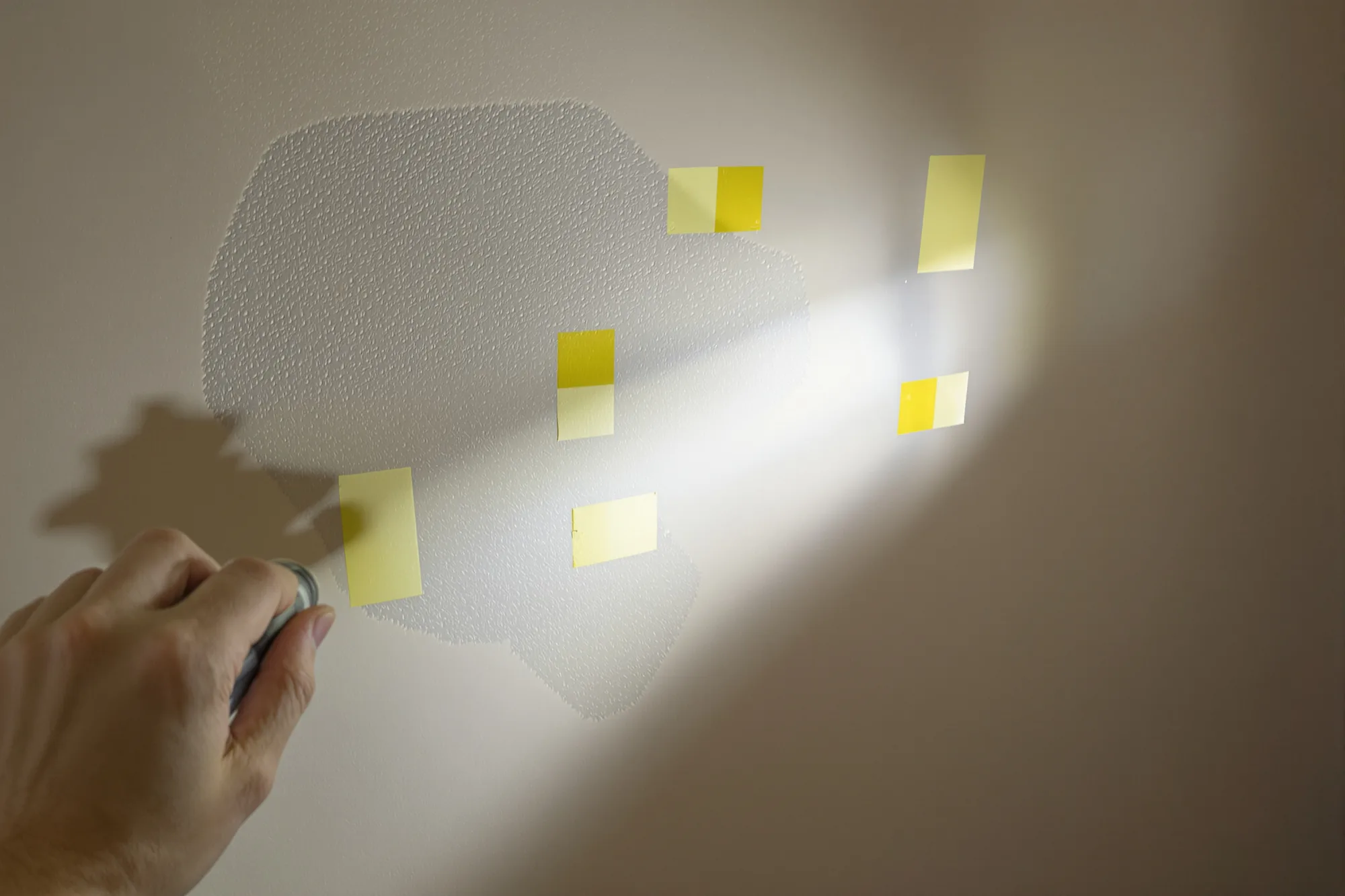 Flashlight held flat against a wall revealing dents, each one marked with a square of tape