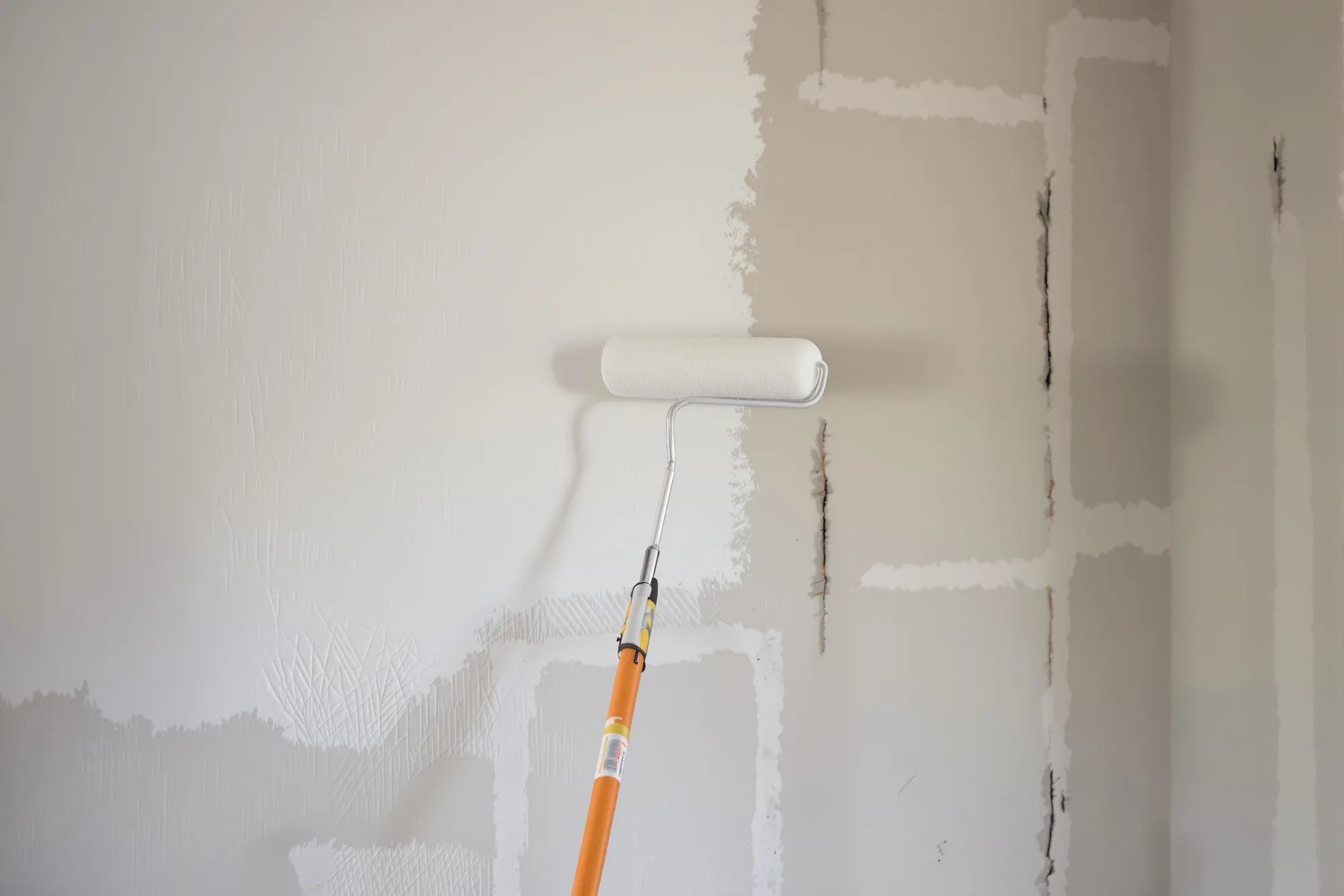 Roller applying white primer to new drywall with taped and mudded seams