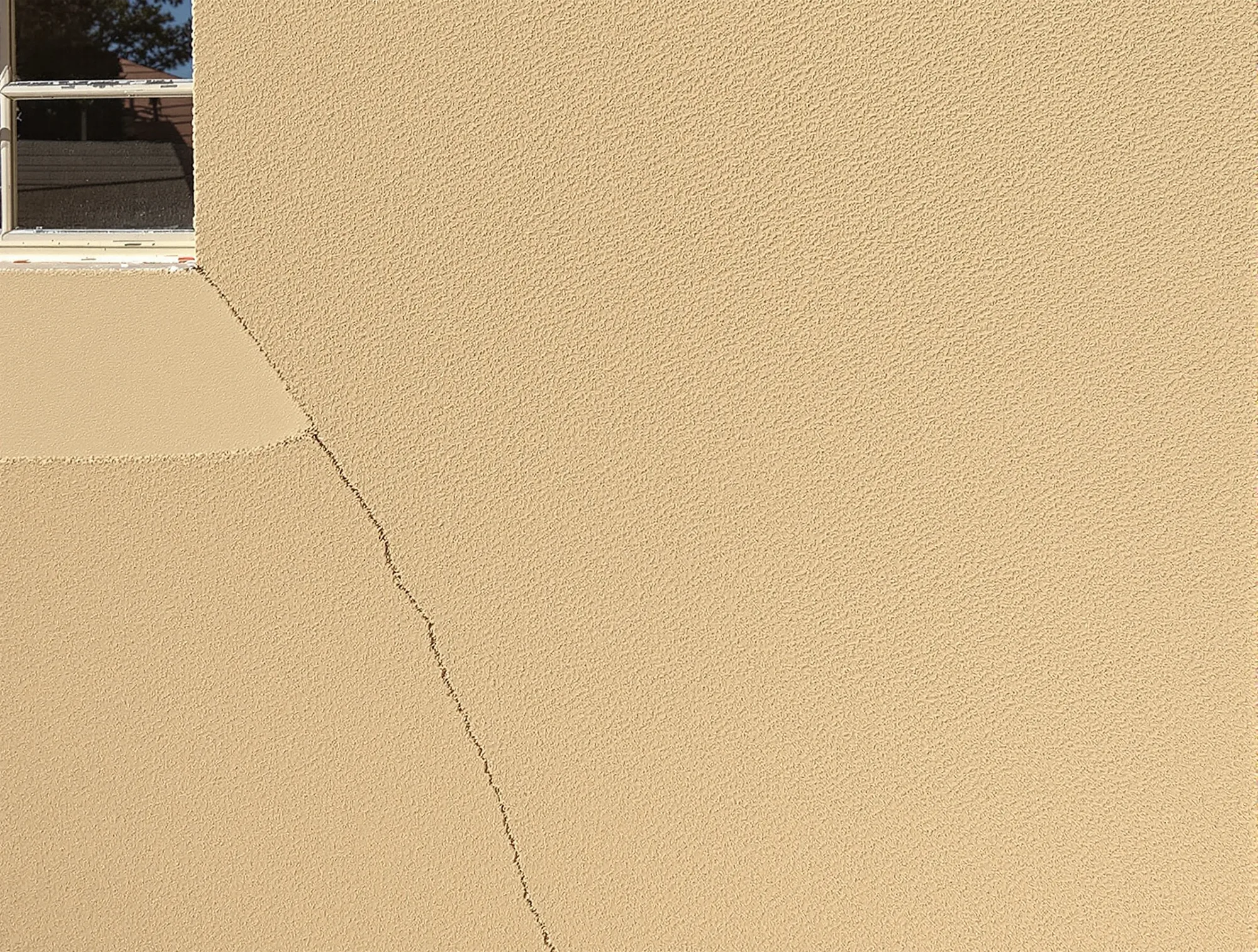 Hairline crack running from a window corner through tan sand finish stucco