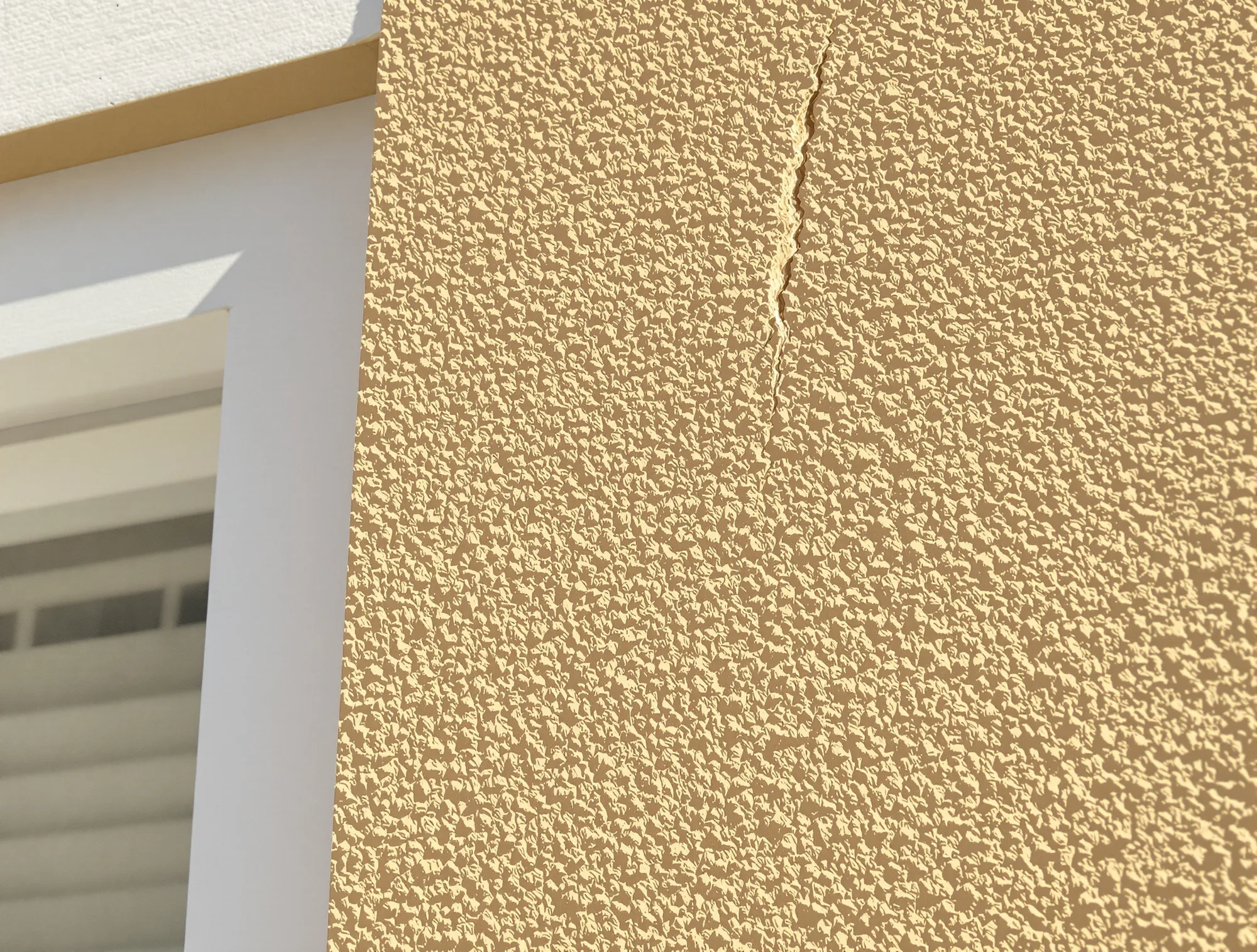 Diagonal crack running from the corner of a window across a tan stucco wall