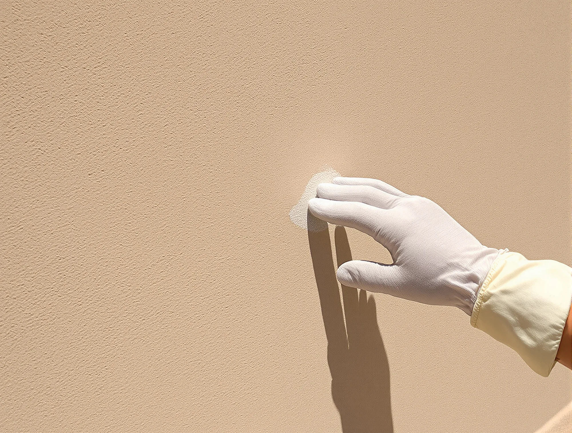 Gloved hand running across a faded stucco wall to check for chalking